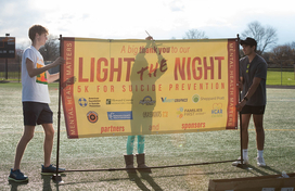 Image of student adjusting a large banner that reads "Light the Night 5K for Suicide Prevention"