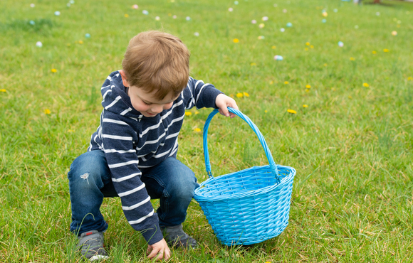 Image of a small boy picking up an easter egg in grass