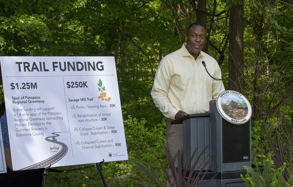 Calvin Ball at a podium with trail funding poster