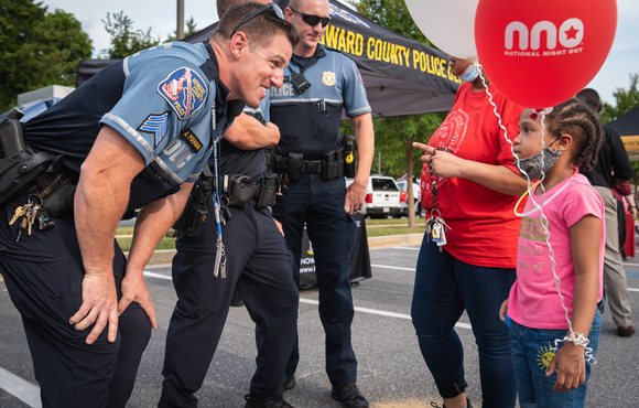 Uniformed officers interact with young girl holding a National Night Out Balloon