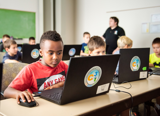 children sitting at desks using laptops