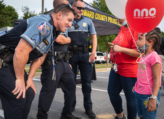 Uniformed officers interact with young girl holding a National Night Out Balloon