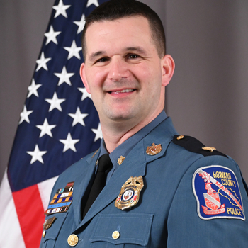 Major Justin Baker in front of flag`